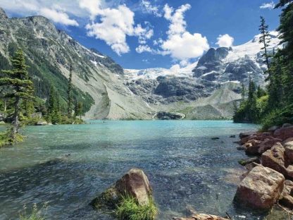 British Columbia Wallpaper is a photo mural of mountains towering over a turquoise lake and pine forest in Joffre Lakes, BC, Canada from About Murals.