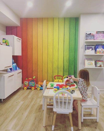 Colorful Wood Wallpaper, as seen on the wall of this rainbow colored kids room, is a mural with blue, purple, pink, red, orange, yellow, green and turquoise planks from About Murals.