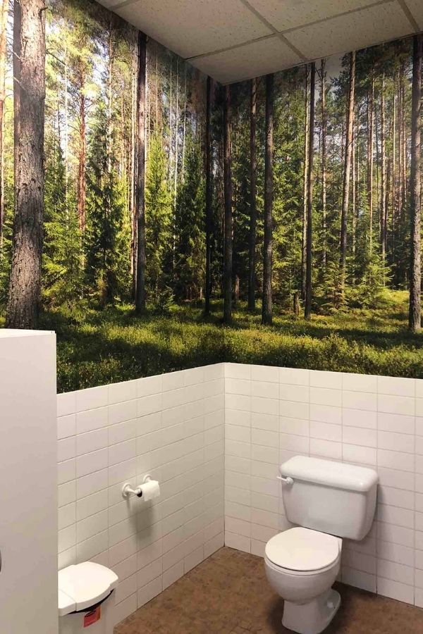 Fir Wallpaper, as seen on the wall of this forest themed bathroom, is a photo mural of evergreen trees against a blue sky from About Murals.