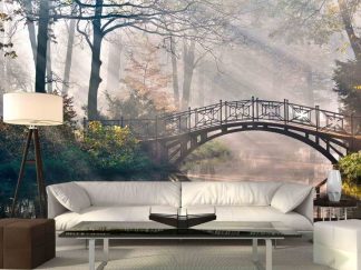 Old Bridge Wallpaper, as seen on the wall of this living room, is a photo mural of sunbeams streaming through autumn trees over an arch bridge and river from About Murals.