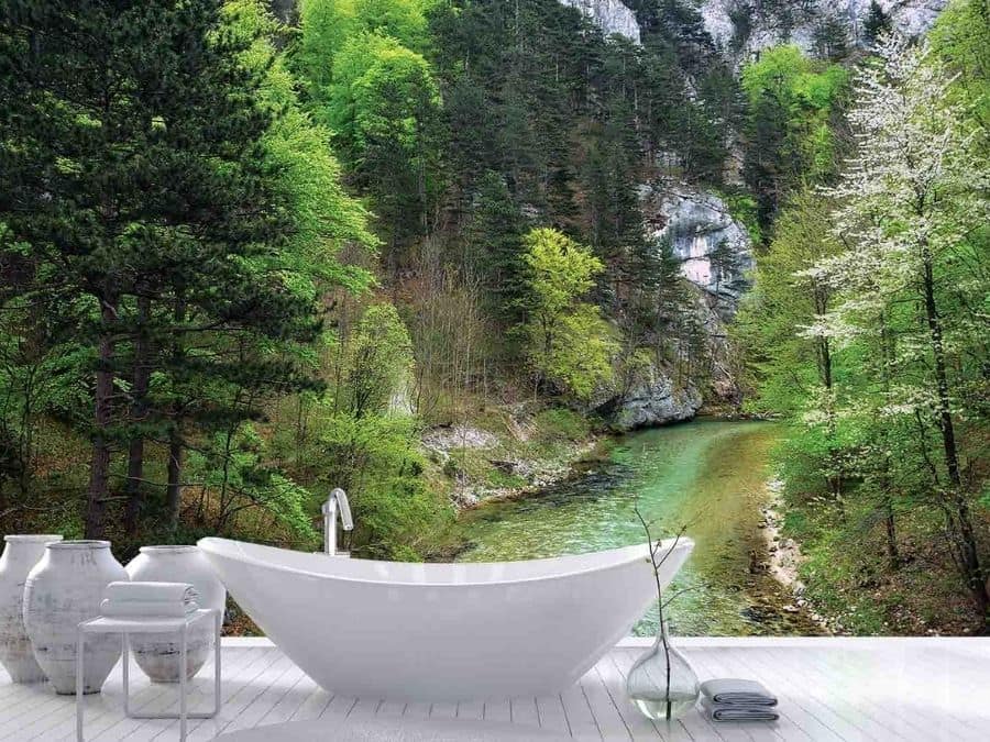 River Wallpaper, as seen on the wall of this nature themed bathroom, is a photo mural of a stream flowing through a pine tree forest near a mountain face from About Murals.