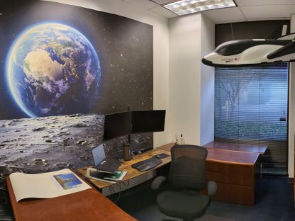 Space Earth Wallpaper, as seen on the wall of this office, is a mural with views of the earth from the moon surrounded by a dark star-studded galaxy from About Murals.