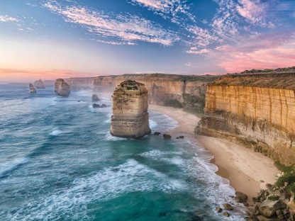 Twelve Apostles Wallpaper is a photo mural of a blue and pink sky over limestone cliffs, the beach and sea in Australia from About Murals.