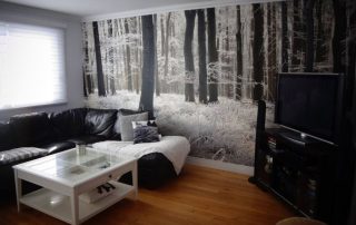 White Forest Wallpaper, as seen on the wall of this black living room, is a photo mural of dark trees contrasted in white snow covered woods from About Murals.