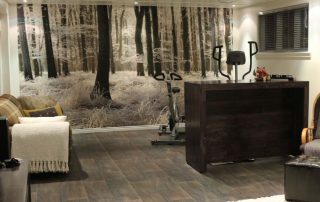 White Forest Wallpaper, as seen on the wall of this home gym, is a photo mural of tall trees covered in snow from About Murals.