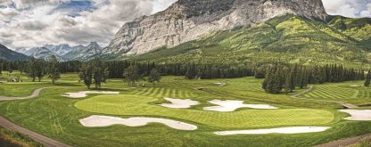 Golf Course Wallpaper is a photo mural of a mountain towering over bunkers and greens dotted with pine trees from About Murals.