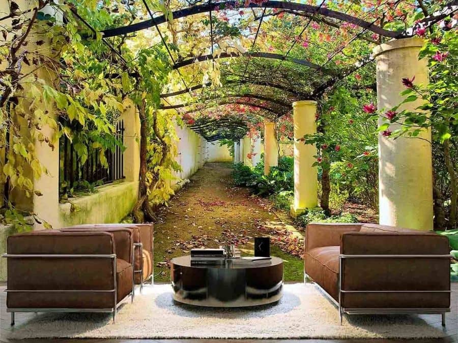 Courtyard Wallpaper, as seen on the wall of this living room, is a photo mural of green vines and pink flowers over a pergola in a garden in Western Cape, South Africa from About Murals.