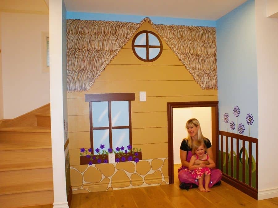 A painted mural in Burlington, ON of a playhouse in a kids playroom created by muralist Adrienne of About Murals.