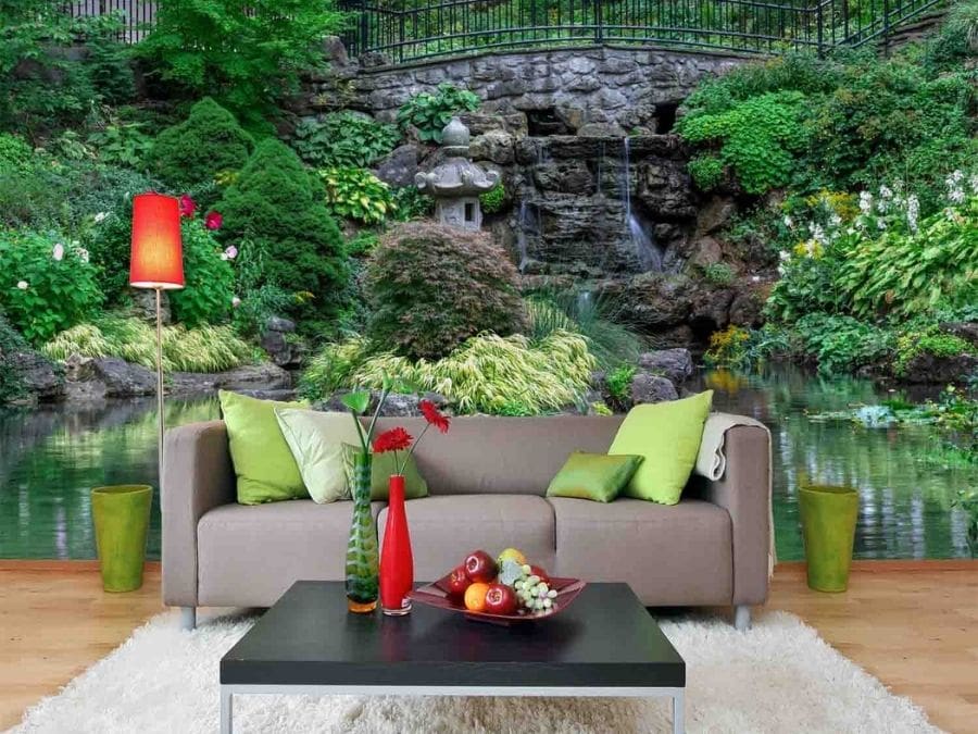 Garden Pond Wallpaper, as seen on the wall of this living room, is a photo mural of a bridge over a waterfall surrounded by a Japanese pagoda statue, plants, flowers and trees from About Murals.
