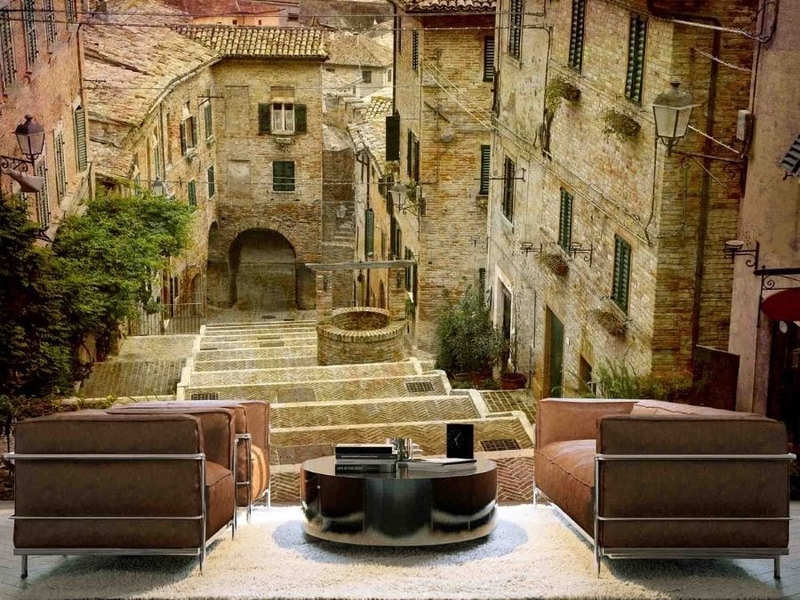 Italian Village Wallpaper, as seen on the wall of this living room, is a photo mural of stairs leading down to a well past old rustic houses from About Murals.