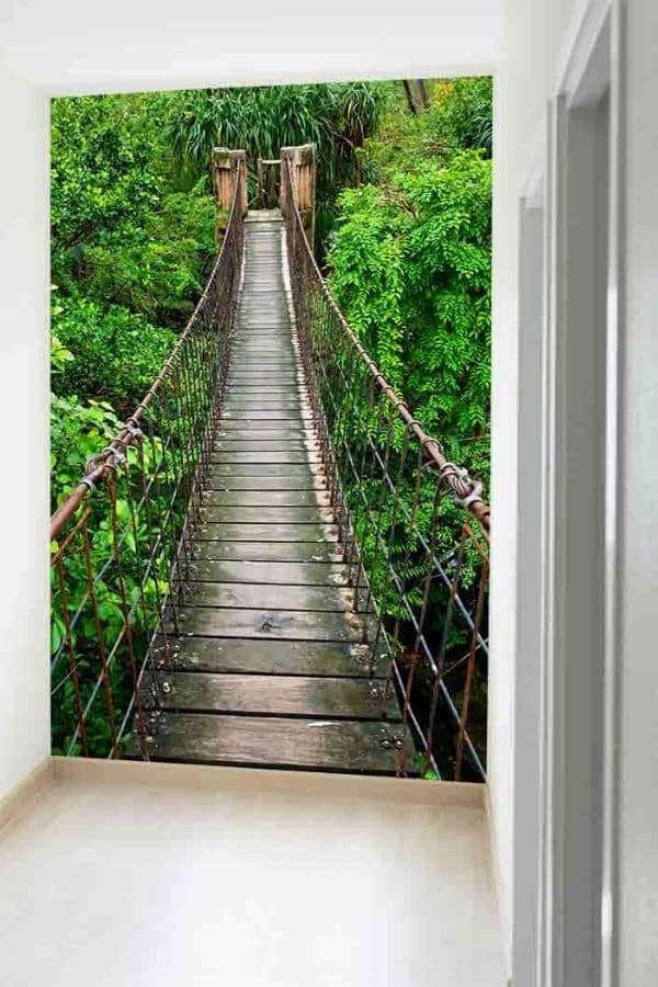 Rope Bridge Wallpaper, as seen on the wall of this hallway, is a photo mural of an old rope walkway surrounded by tropical trees in a forest from About Murals.