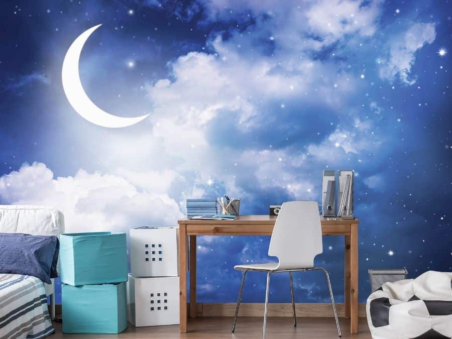 Moon Wallpaper, as seen on the wall of this bedroom, is a wall mural with stars and a crescent moon illuminating dreamy clouds in a night sky from About Murals.
