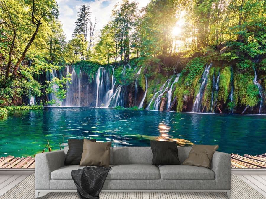 Tropical Waterfall Wallpaper, as seen on the wall of this living room, is a photo mural of a sunset shining through trees over exotic falls spilling into a blue lagoon from About Murals.