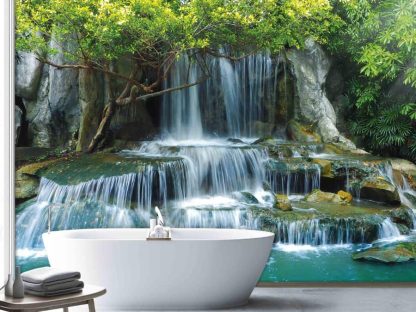 Waterfall Wallpaper, as seen on the wall of this bathroom, is a photo mural of blue water cascading over tiered rocks in a tropical garden from About Murals.