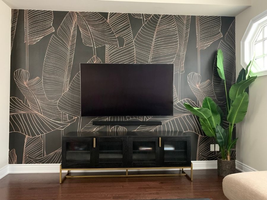 Black and Gold Leaf Wallpaper Mural, as seen in this living room, is a mural with tall gold tropical leaves on a black background from About Murals.