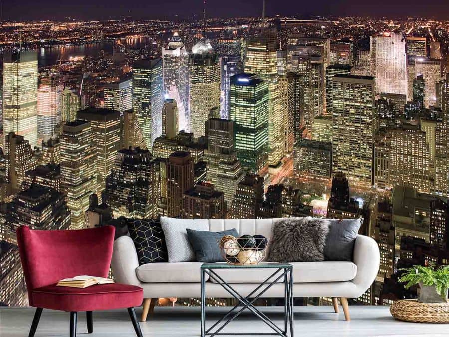 Manhattan at Night Wallpaper, as seen on the wall of this dark living room, is a photo mural of skyscrapers in New York City lit up under a nighttime sky from About Murals.