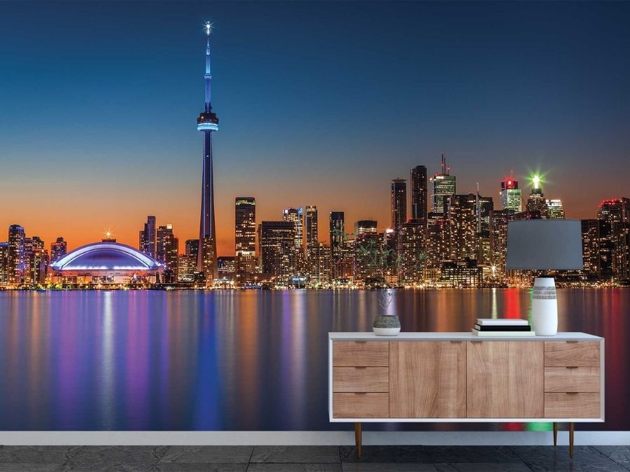 Toronto Skyline Wallpaper, as seen on the wall of this living room, is a photo mural of neon lights on the CN Tower, Rogers Centre and skyscrapers reflected in Lake Ontario against a blue dusk sky from About Murals.