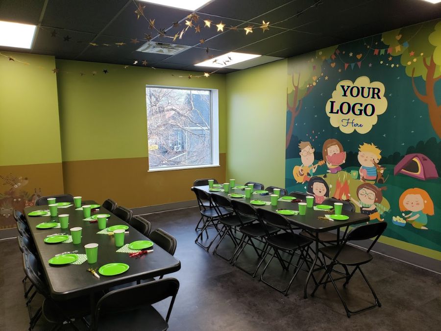 Birthday party venue business, decorated with custom word wallpaper in a camping theme, on the wall behind two tables with paper plates and cups.