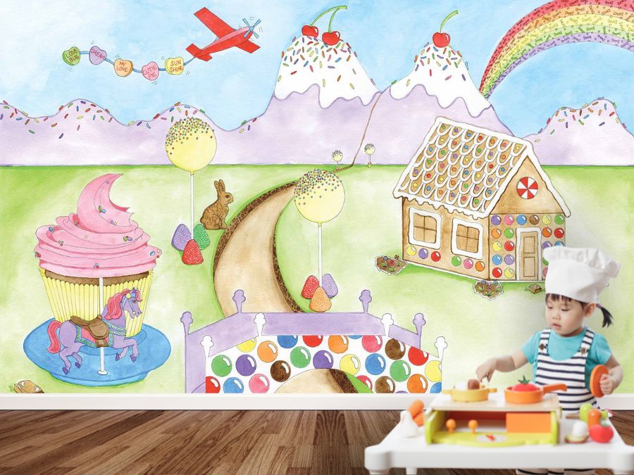 Candy theme indoor playground with a wallpaper mural featuring a cupcake carousel, gingerbread house, ice cream mountains and candy rainbow from About Murals.