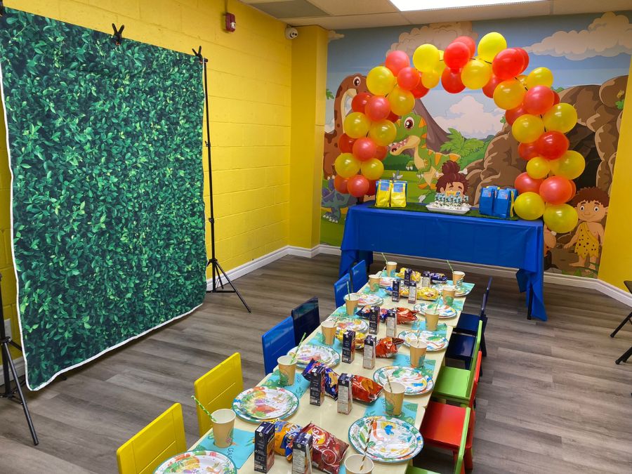Dinosaur indoor playground, with a custom wallpaper on the wall, behind a party table for kids from About Murals.