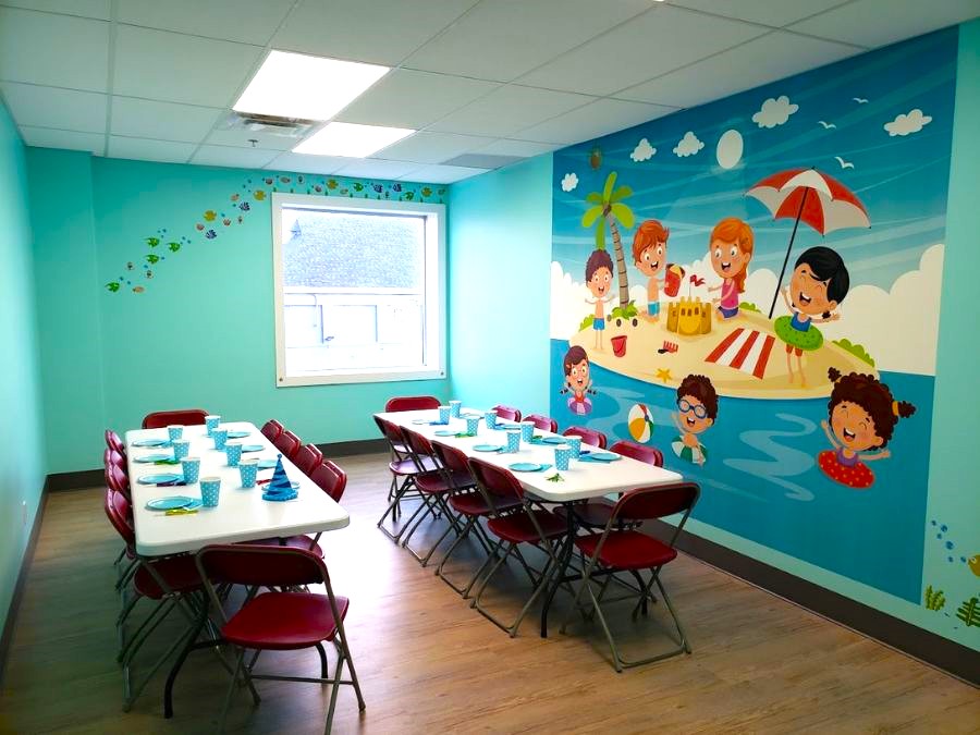Indoor children's playground business wallpaper mural of kids playing on a beach, on a wall behind birthday party tables with plates and party hats.