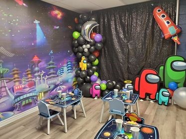 Party space theme in a birthday party room, with an outer space mural from About Murals, planet themed kids tables, birthday party balloons and astronaut decorations.
