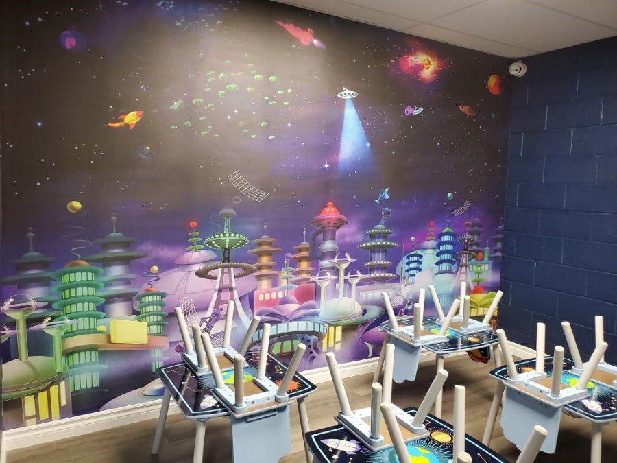 Space themed indoor playground with an outer space wallpaper mural from About Murals and planet themed kids tables.
